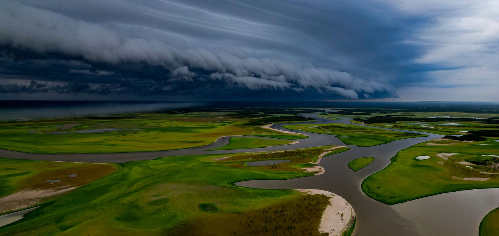 Aerial view of Lake Tefé in the Brazilian Amazon, with low-water channels and exposed sandbanks under a dark shelf cloud bringing the first rains after the 2024 drought