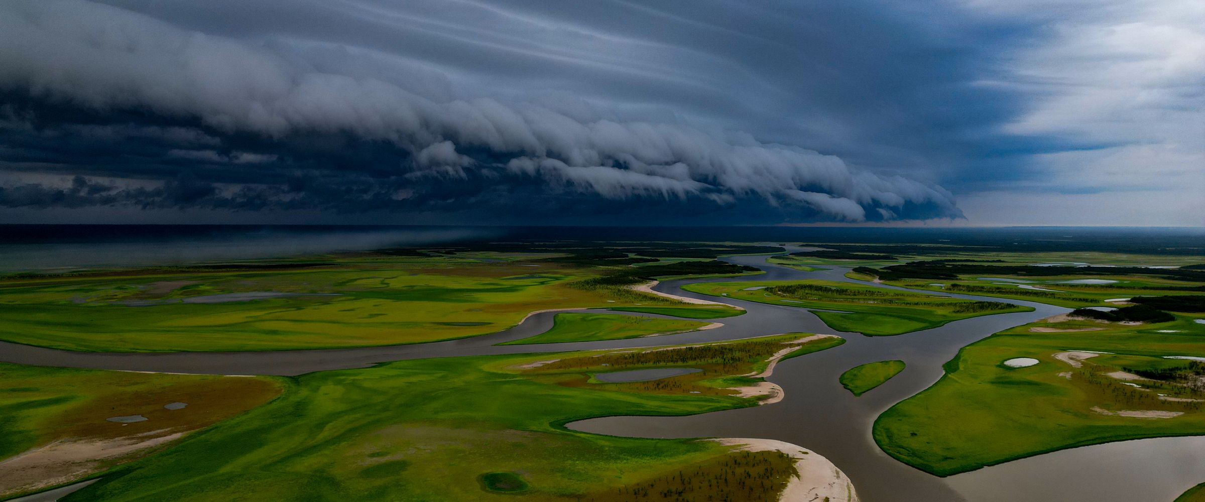 Aerial view of Lake Tefé in the Brazilian Amazon, with low-water channels and exposed sandbanks under a dark shelf cloud bringing the first rains after the 2024 drought